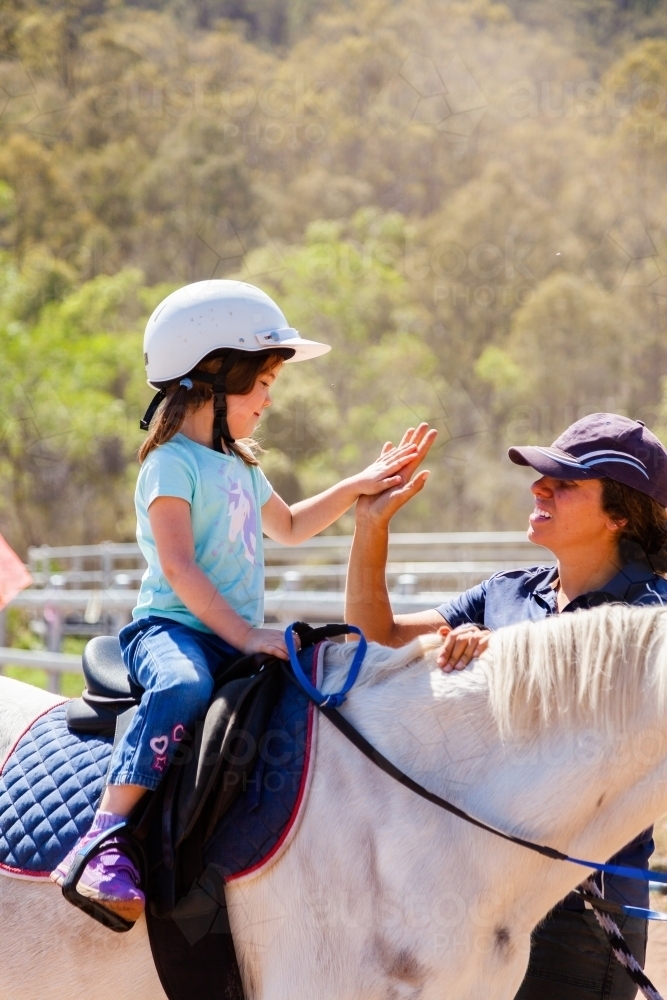 Horse riding instructor giving little girl a high five on horseback - Australian Stock Image
