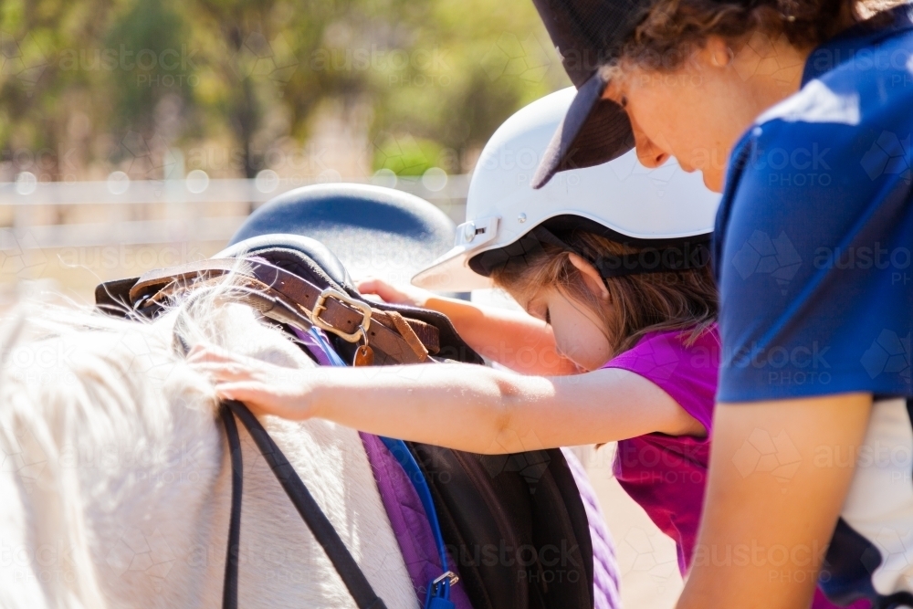 Horse riding instructor helping young student mount pony - Australian Stock Image
