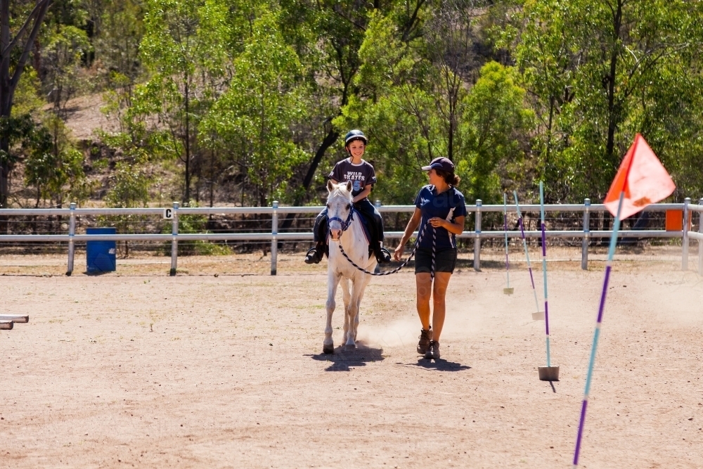 Horse riding instructor leading student on horse for first riding lesson - Australian Stock Image