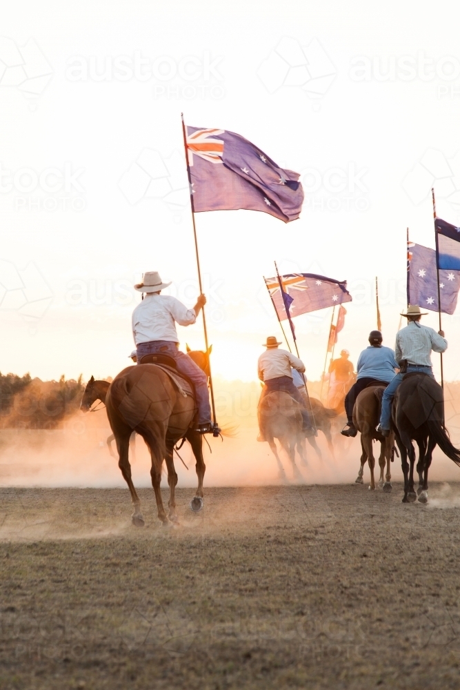 Horsemen with Australian flags riding into dust at sunset - Australian Stock Image