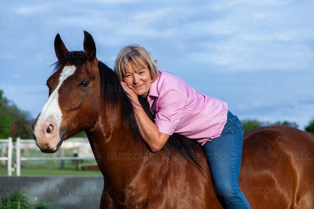 Horsewoman leaning on horses neck while riding bareback - Australian Stock Image