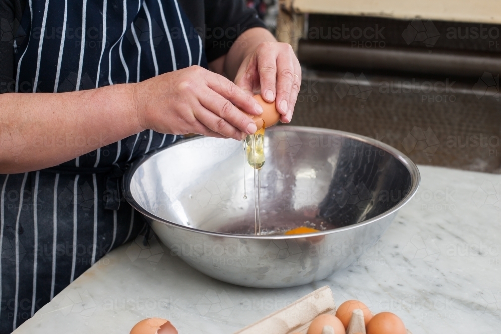 Hospitality worker breaking eggs into a bowl - Australian Stock Image