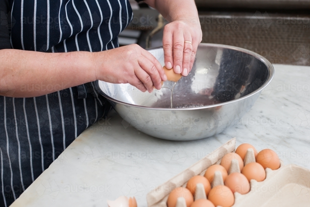 hospitality worker breaking eggs into a bowl - Australian Stock Image