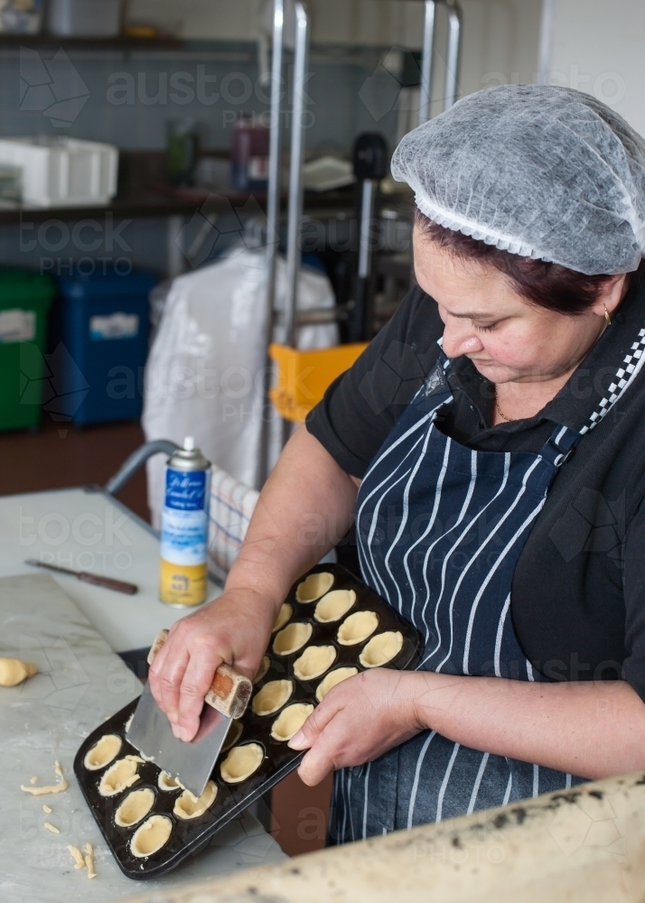 Hospitality worker cutting pastry off a baking tray - Australian Stock Image