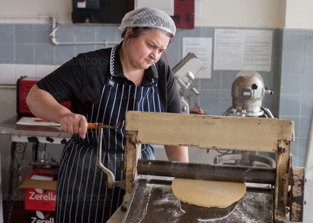 Hospitality worker running dough through a pastry roller - Australian Stock Image