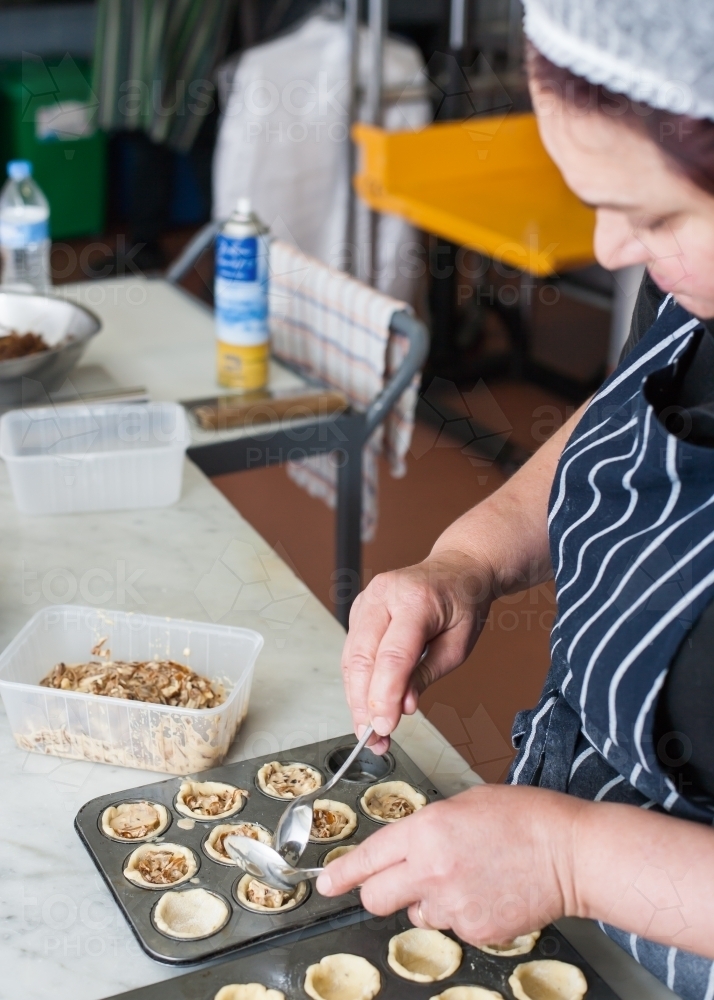 hospitality worker spooning mixture into pastry shells - Australian Stock Image