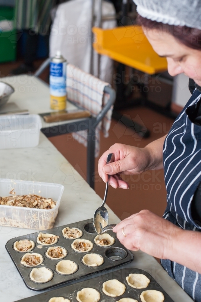 hospitality worker spooning mixture into pastry shells - Australian Stock Image