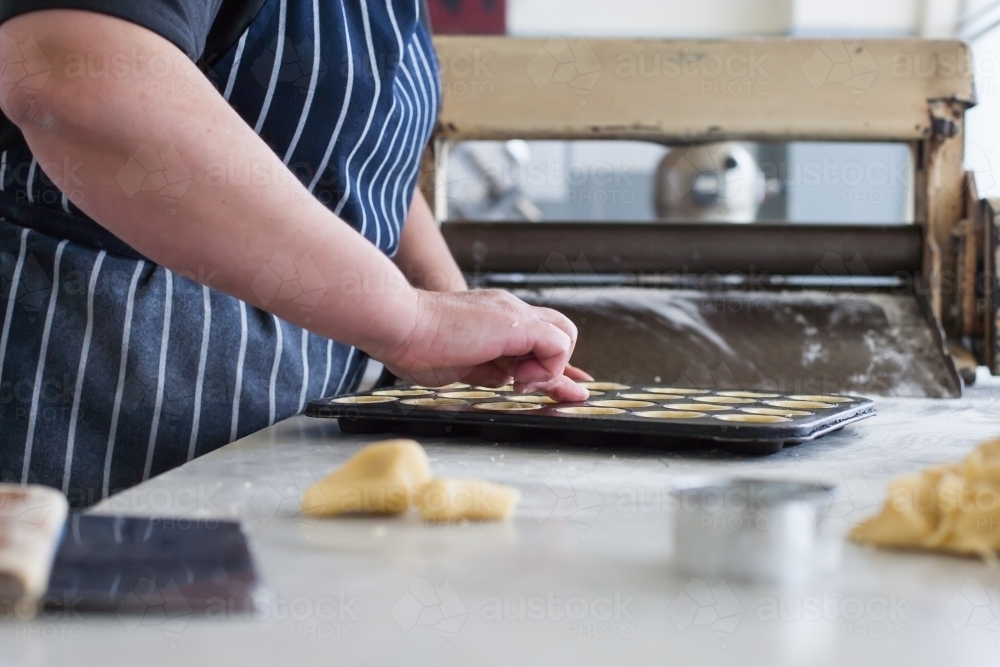 Image of Hospitality worker working pastry into a baking tray ...