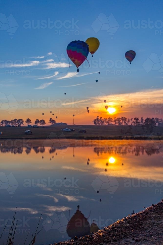Hot air balloons reflected over lake on a colourful sunrise - Australian Stock Image