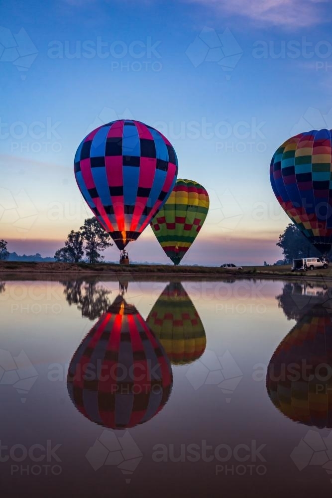 Hot air balloons taking off and reflected over lake at sunrise - Australian Stock Image
