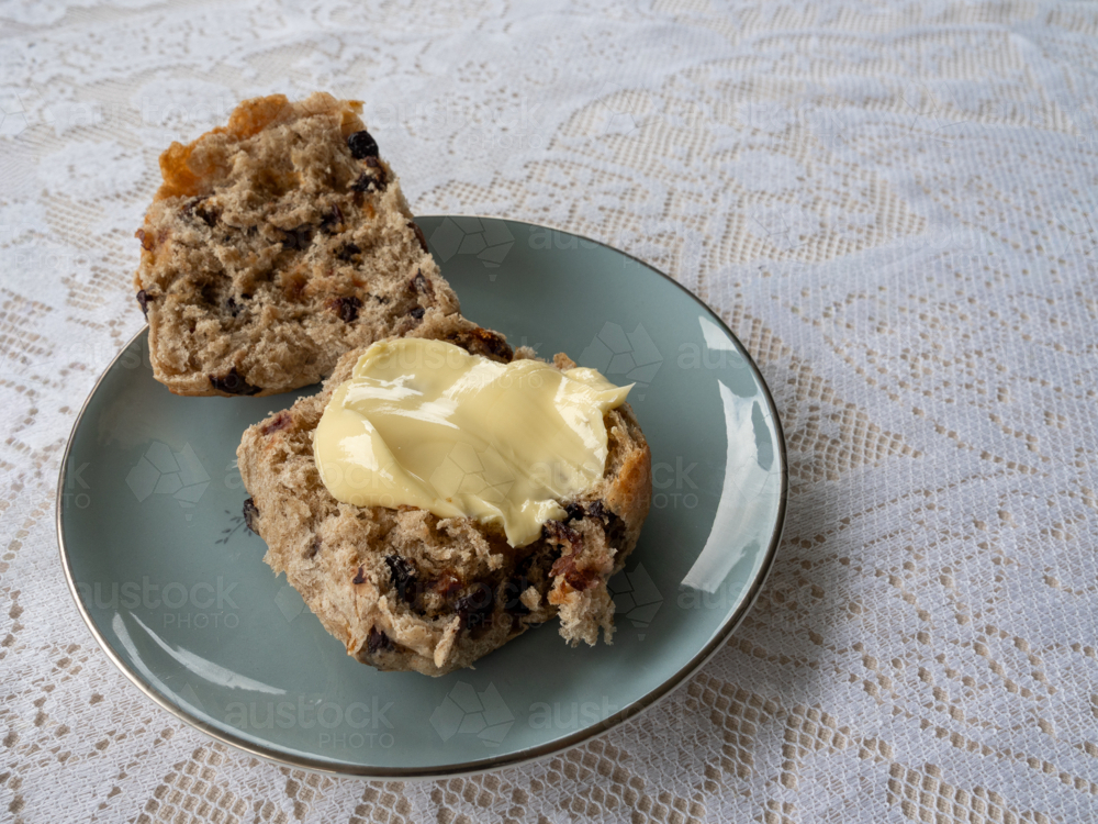 Hot cross bun with butter on a blue plate with lace table cloth - Australian Stock Image