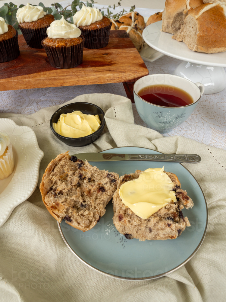Hot cross buns and carrot cake on wooden platter with cup of tea and linen napkin - Australian Stock Image