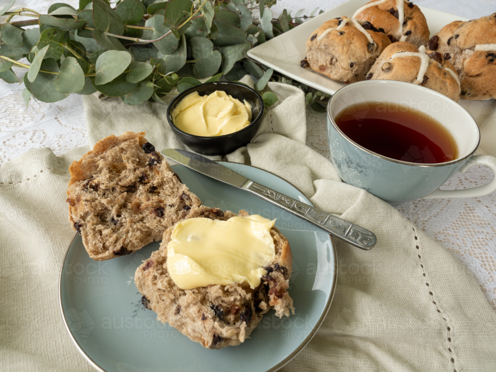 Hot cross buns with butter on linen napkin with cup of tea and eucalyptus branch - Australian Stock Image