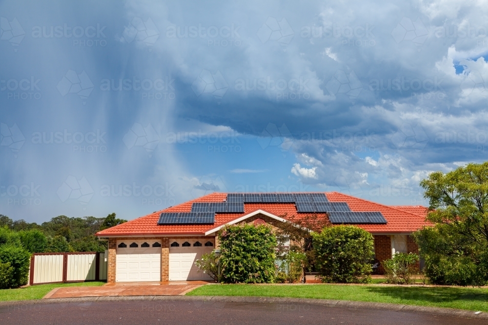 House with solar panels on the roof and rain clouds behind it - Australian Stock Image