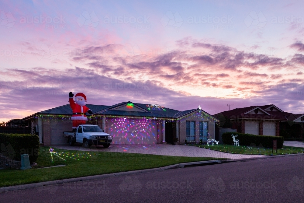 Houses displaying festive Christmas lights at dusk on suburban street - Australian Stock Image