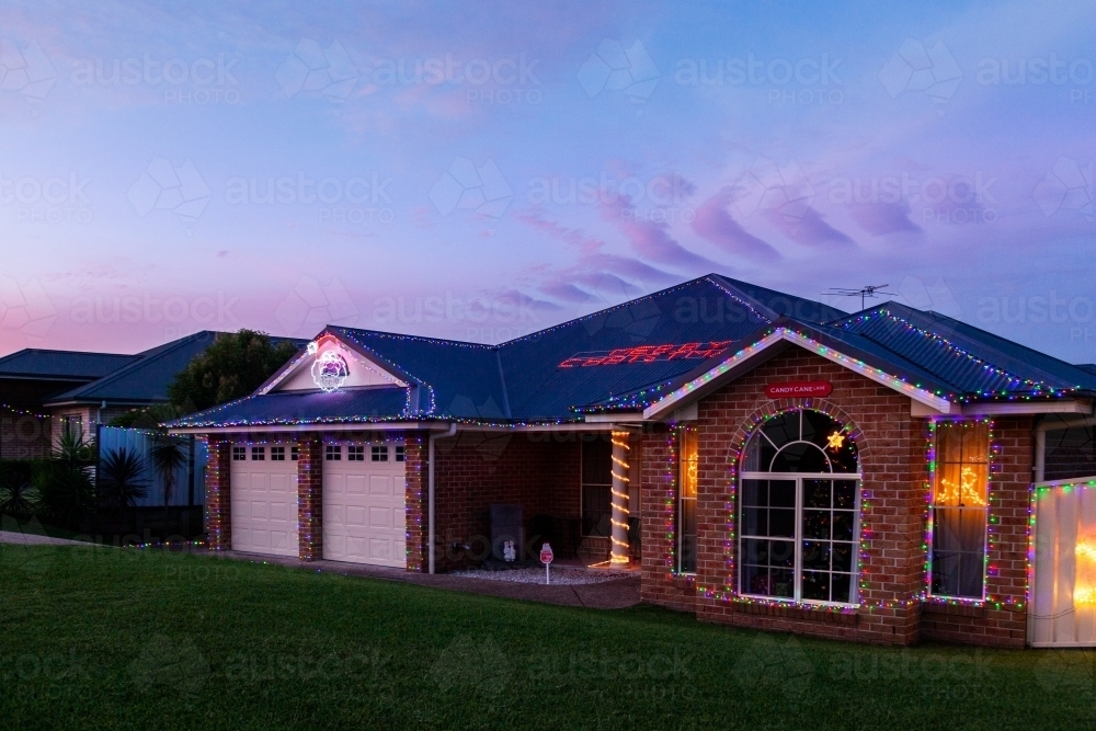 Houses displaying festive Christmas lights at dusk on suburban street - Australian Stock Image