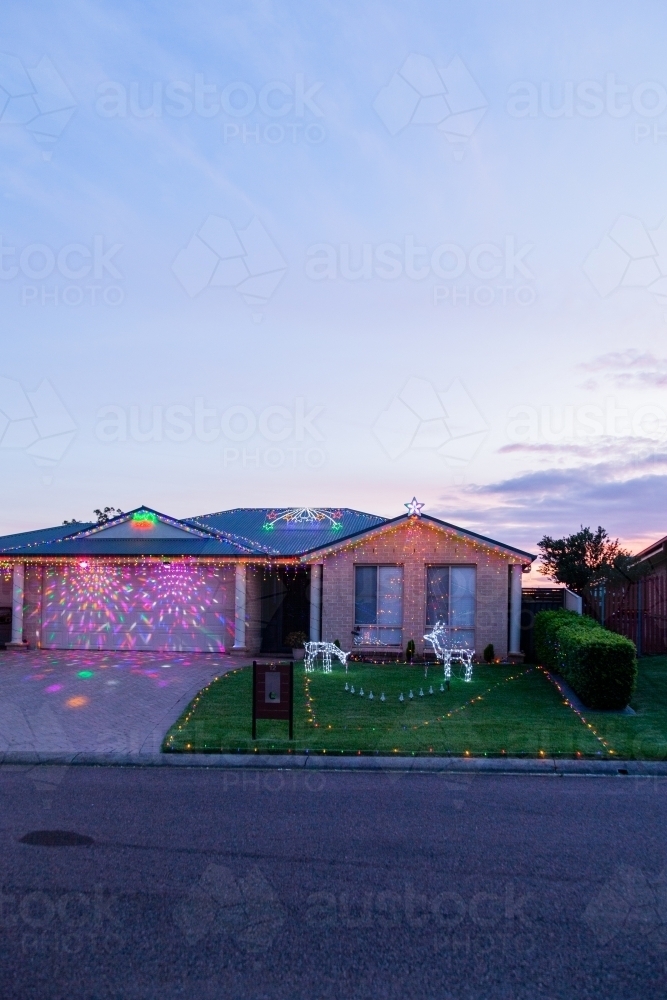 Houses displaying festive Christmas lights at dusk on suburban street - Australian Stock Image