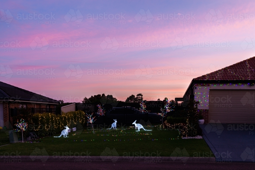 Houses displaying festive Christmas lights with kangaroo figures at dusk on suburban street - Australian Stock Image