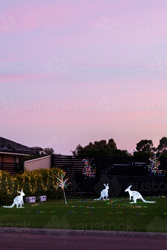 Houses displaying festive Christmas lights with kangaroo figures at dusk on suburban street - Australian Stock Image