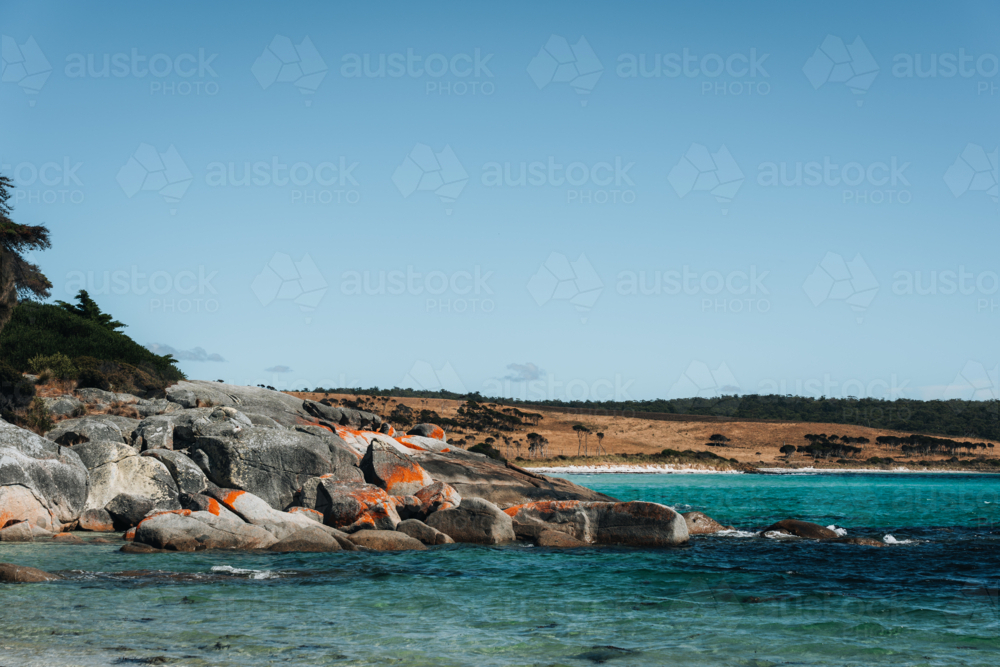 Huge reddish rocks along the shoreline with blue waters - Australian Stock Image