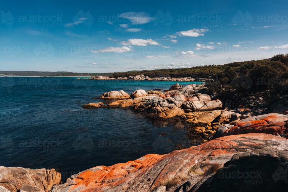 Huge reddish rocks along the shoreline with blue waters - Australian Stock Image