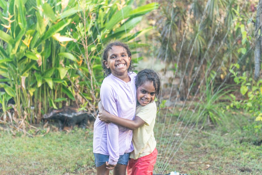 Hugging aboriginal sisters having water play - Australian Stock Image