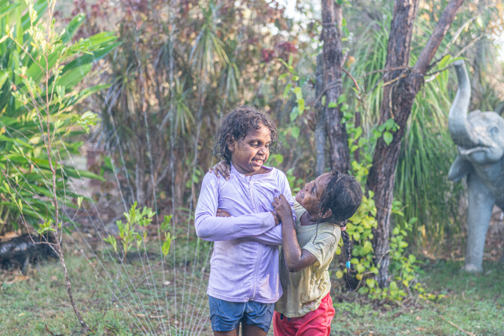 Hugging aboriginal sisters having water play - Australian Stock Image