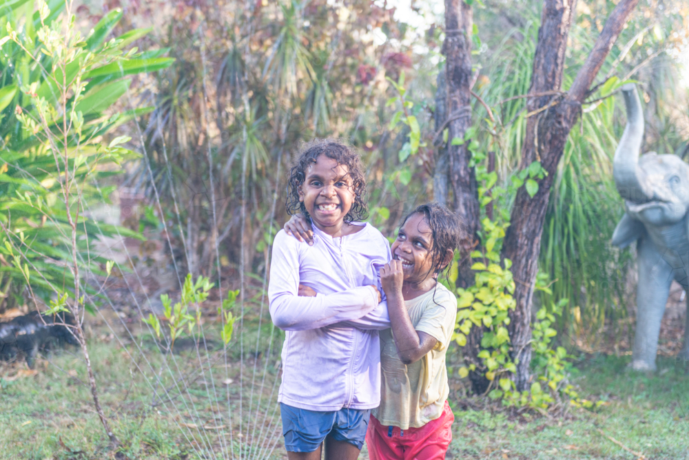 Hugging aboriginal sisters having water play - Australian Stock Image