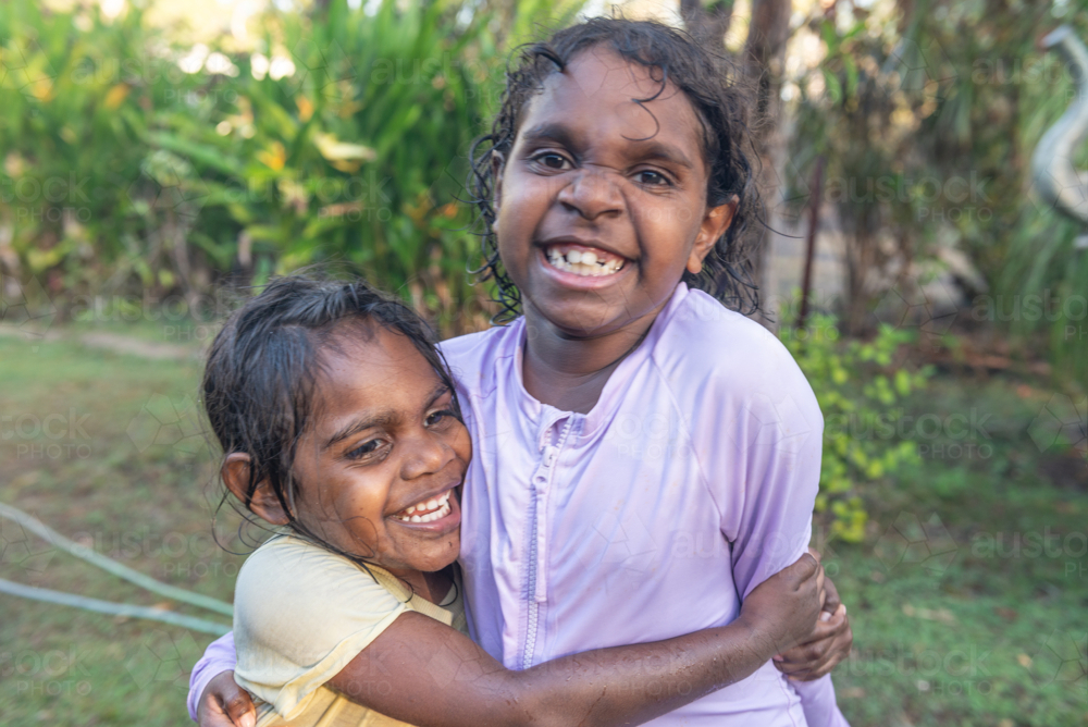 Hugging aboriginal sisters having water play - Australian Stock Image
