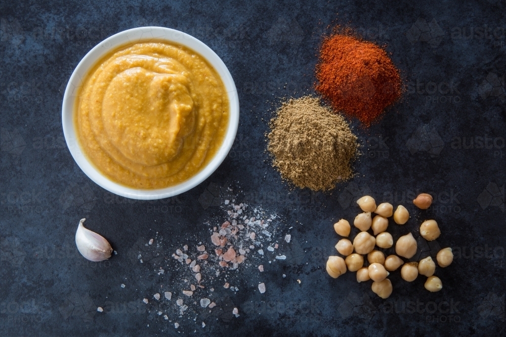 Hummus served in small white bowl with Chick Peas and spices, on a blue background - Australian Stock Image