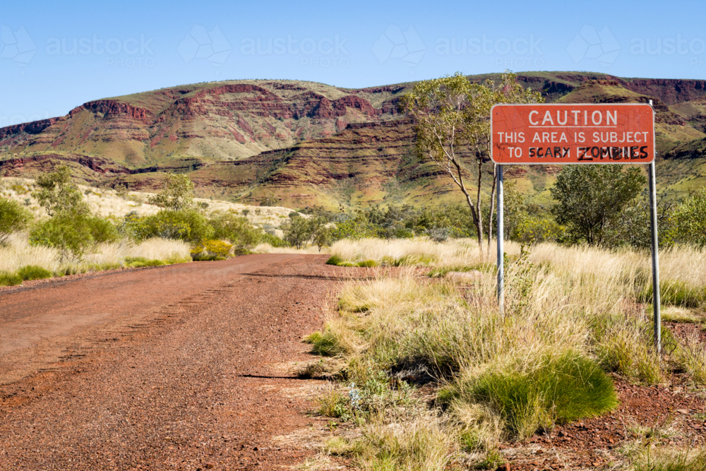 Humorous road sign warning of zombies on remote outback road near red rock ranges. - Australian Stock Image