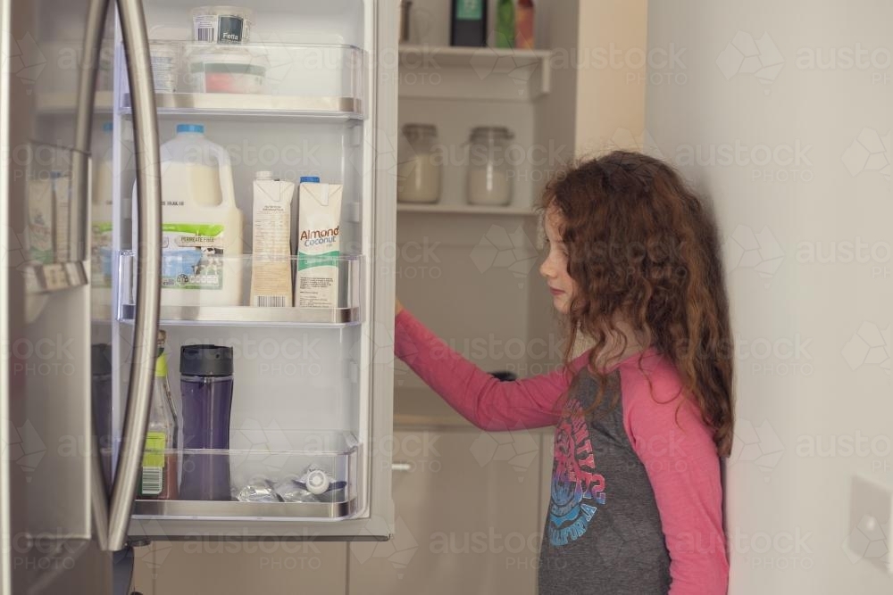 Hungry growing girl looking for food in fridge - Australian Stock Image