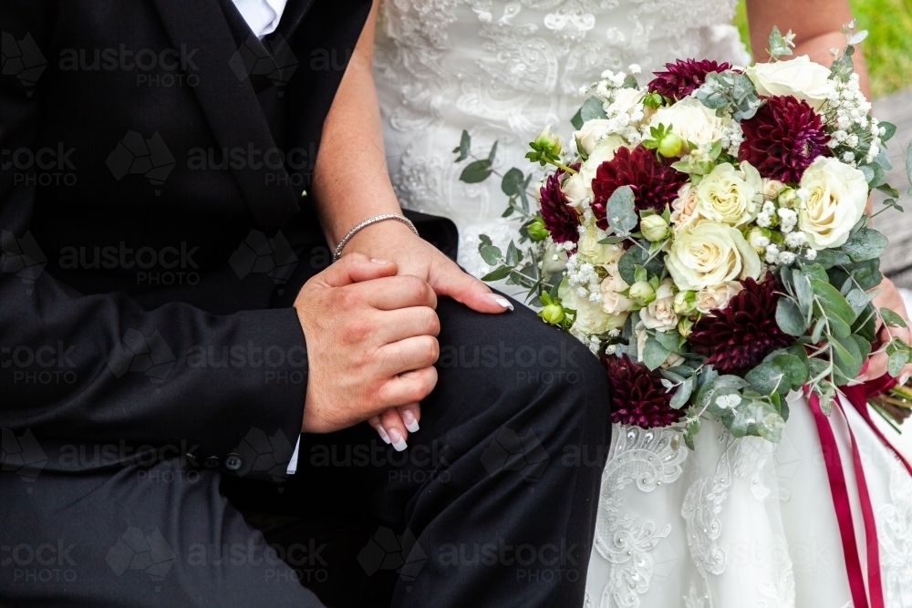 Husband and wife holding hands on wedding day with flower bouquet - Australian Stock Image
