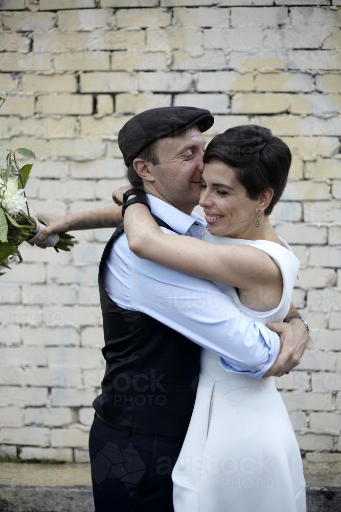 Husband and wife hugging and kissing on wedding day - Australian Stock Image