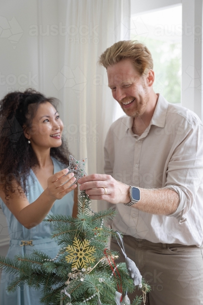Husband and wife placing star on Christmas tree together - Australian Stock Image