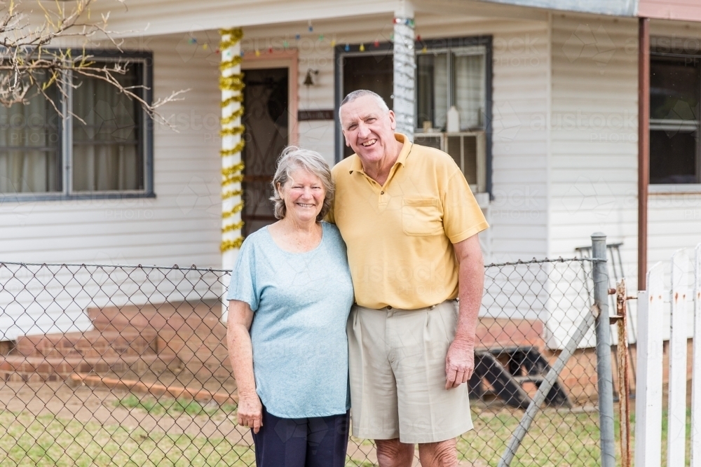 Husband and wife retired older couple standing arm in arm in front of house happy - Australian Stock Image