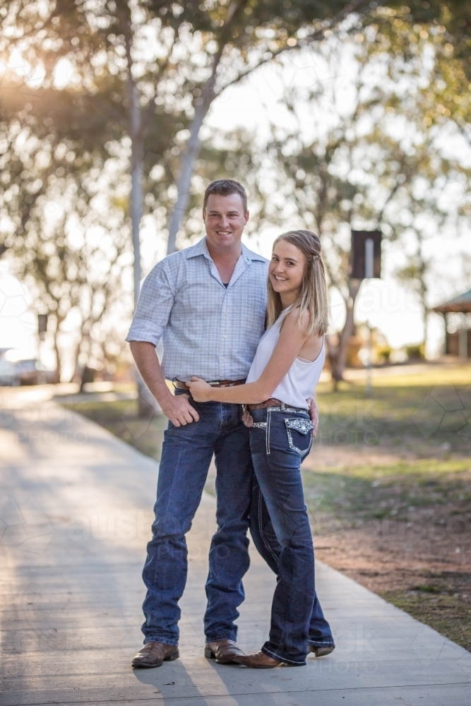 Husband and wife standing close together on path at park smiling - Australian Stock Image