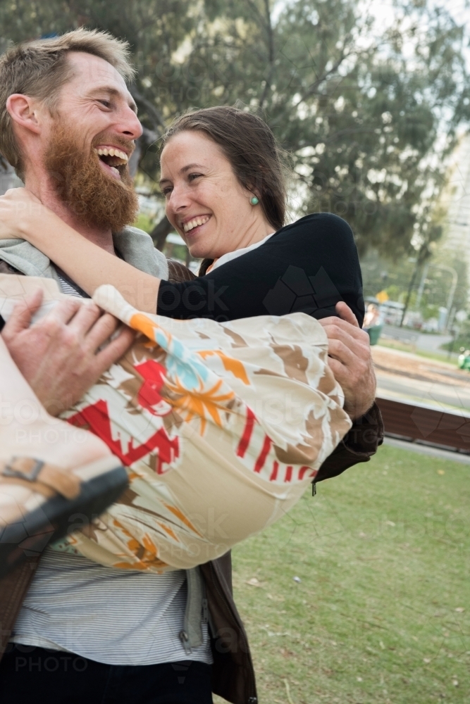 Husband holding his wife in his arms while they both laugh. - Australian Stock Image