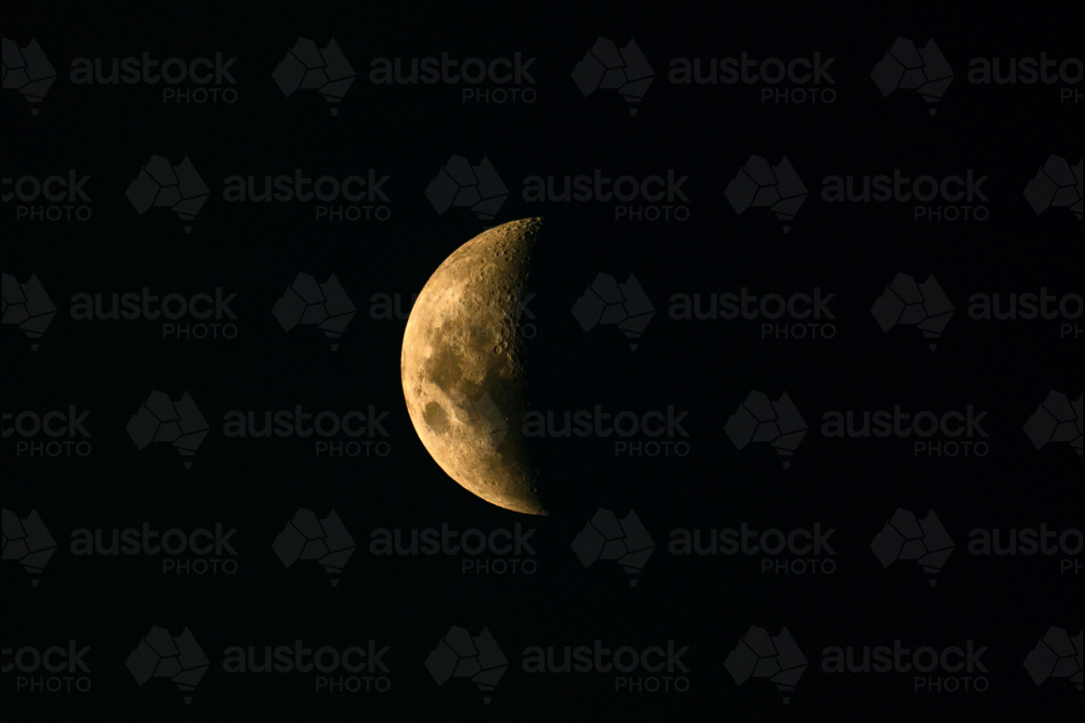 Illuminated moon surface showing visible craters and rugged textures against the black night sky - Australian Stock Image