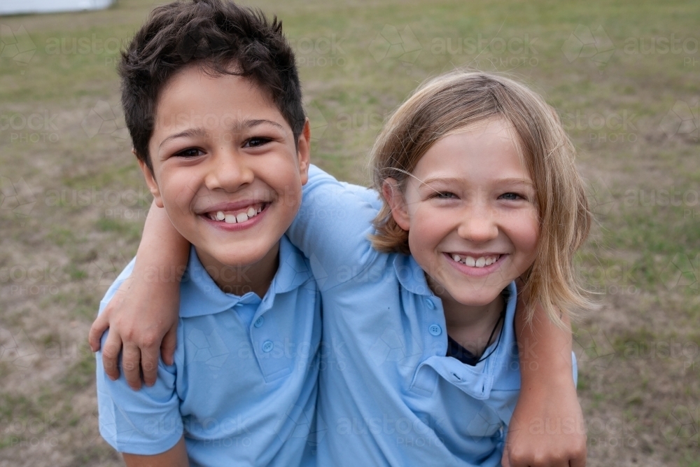 Close up of two smiling school kids with arms around each other - Australian Stock Image