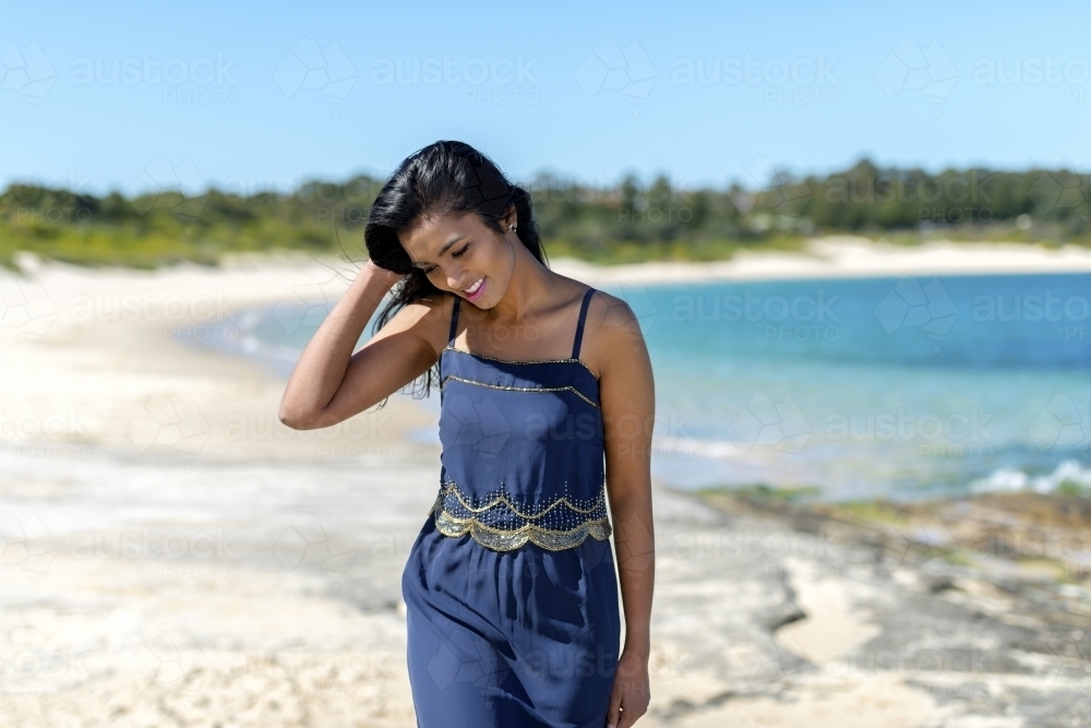 Indian woman smiling whilst walking on beach - Australian Stock Image