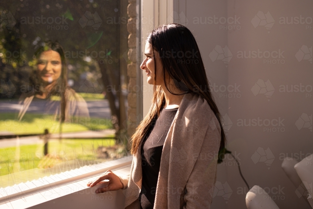 Woman Standing In Window Image of Indian woman standing by the window looking outside on a sunny ...