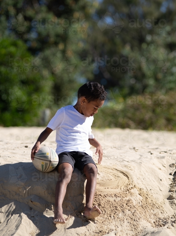 Indigenous boy playing on a sand ledge with ball - Australian Stock Image