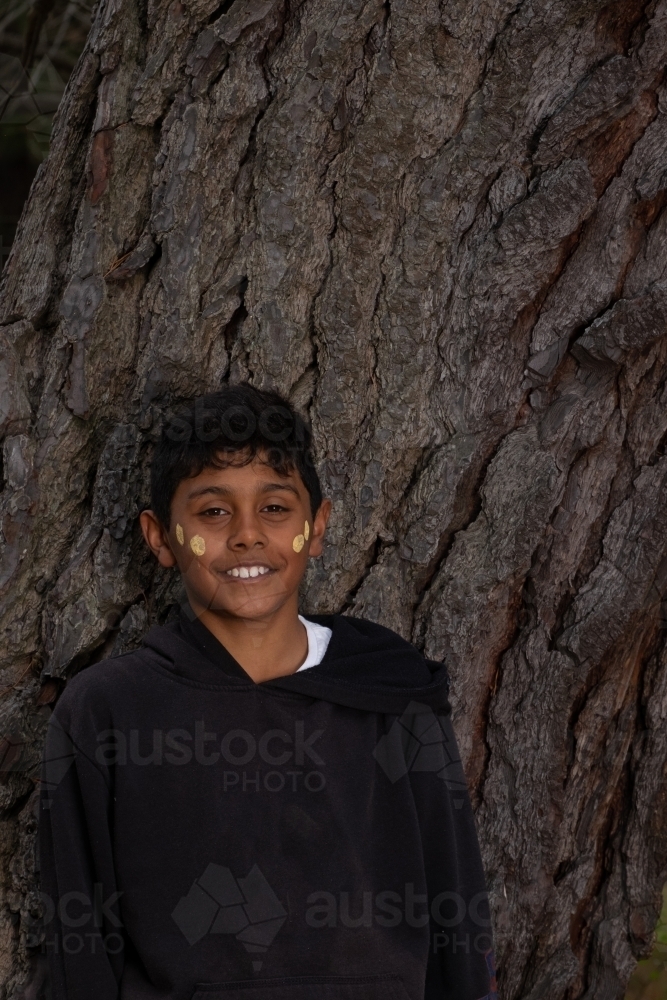 Indigenous boy standing near an old tree trunk - Australian Stock Image