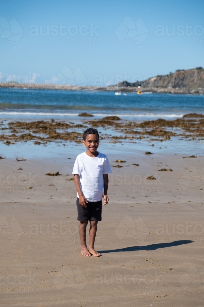 Indigenous boy standing on the sand at a beach - Australian Stock Image