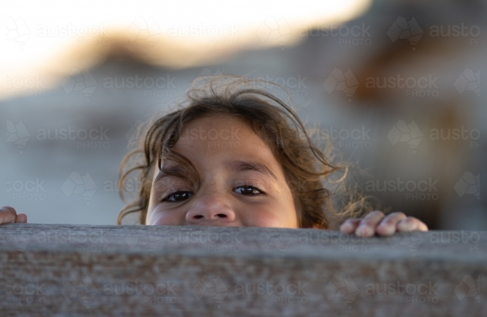 Indigenous girl peeping over wooden fence - Australian Stock Image