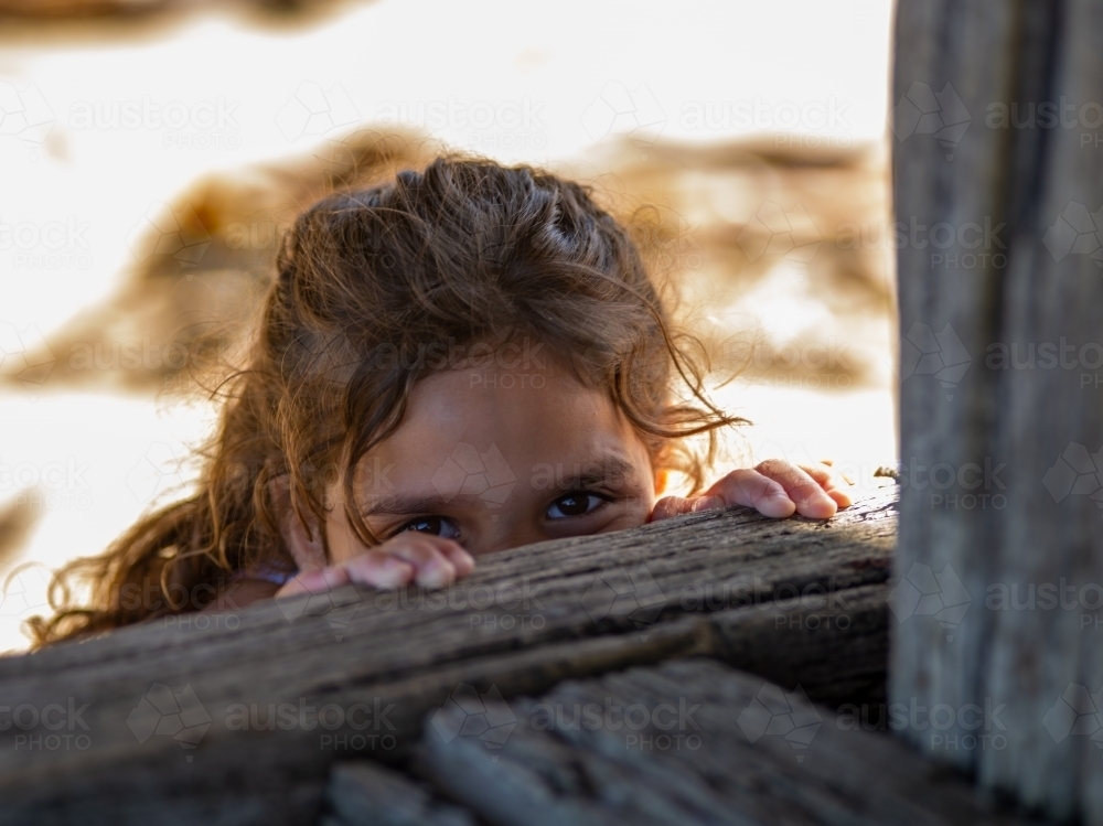 Indigenous girl peeping over wooden fence - Australian Stock Image