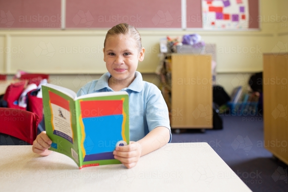 Indigenous girl primary school student with a book in a classroom - Australian Stock Image