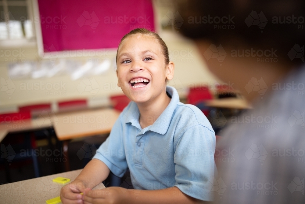 Indigenous girl school student laughing with a friend in a classroom - Australian Stock Image