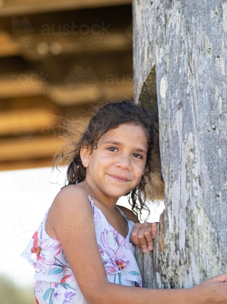 Indigenous girl standing against a wooden pole - Australian Stock Image